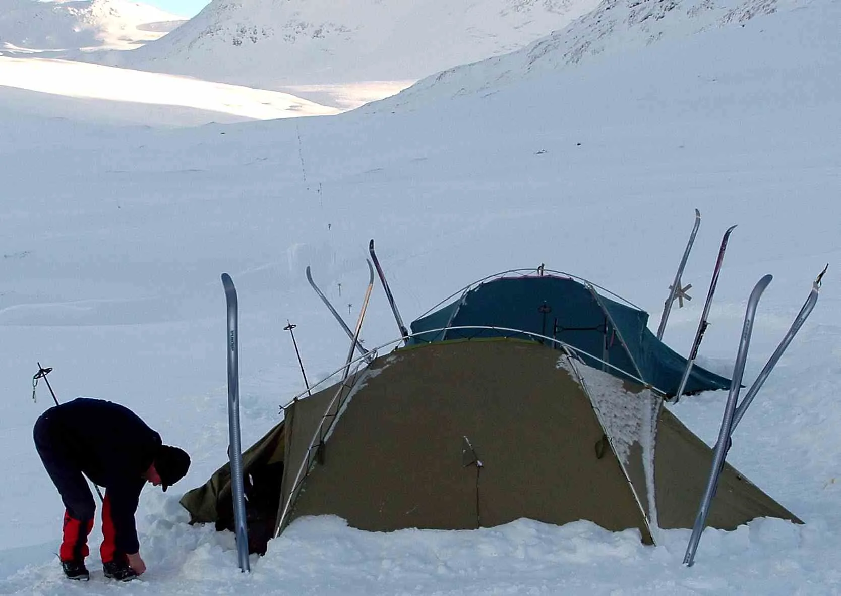 Campamento de dos tiendas dug en la nieve con esquís clavados alrededor, en las montañas de Suecia