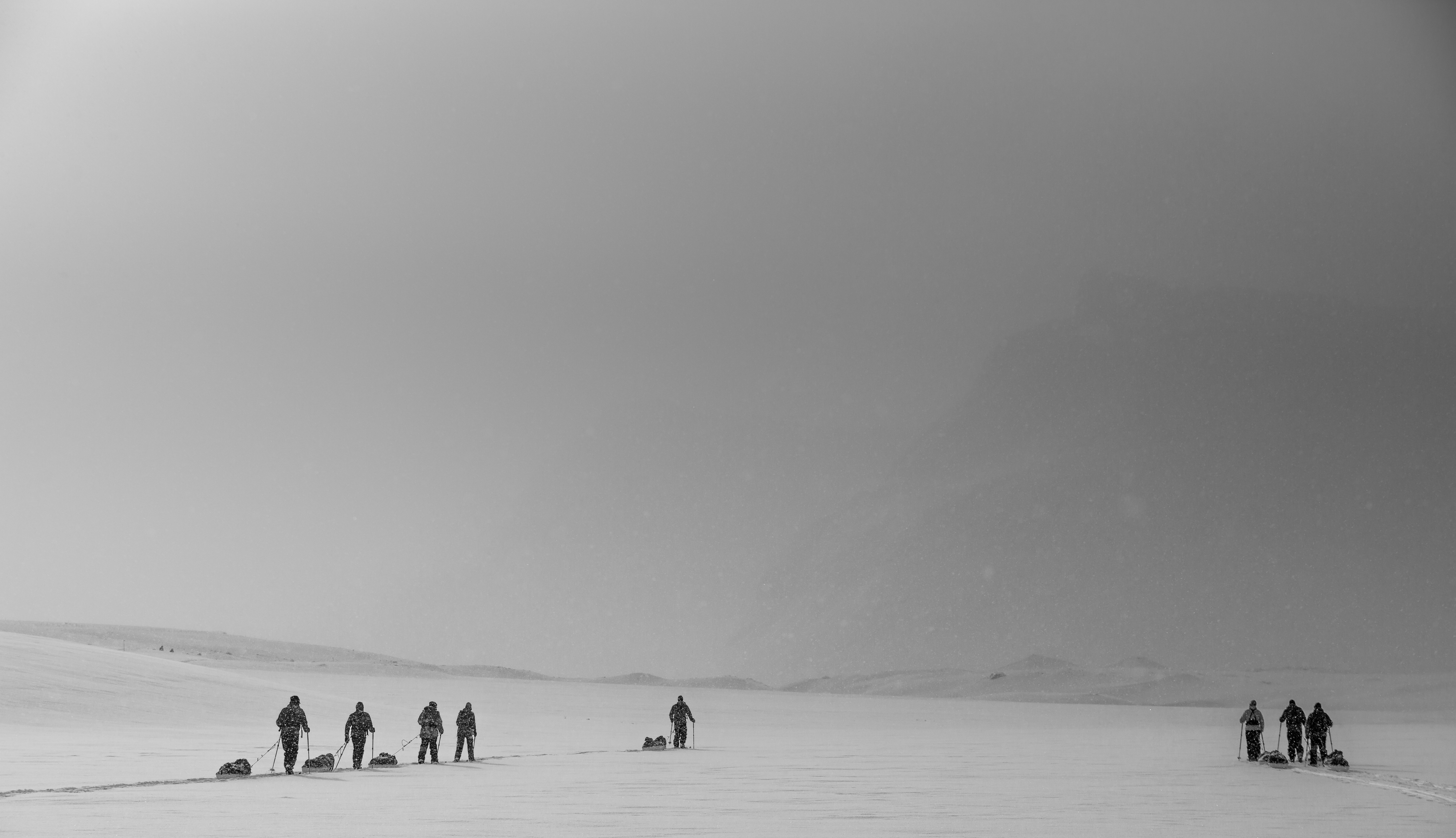 Grupo de expedicionarios cruzando un paisaje ártico con esquís y pulka en plena nevada