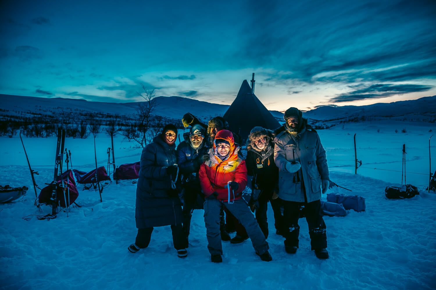 Grupo de expedicionarios junto a un tipi de nieve al anochecer en Laponia