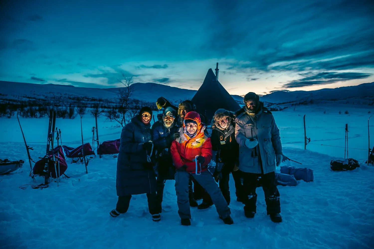 Grupo de expedicionarios junto a un tipi de nieve al anochecer en Laponia