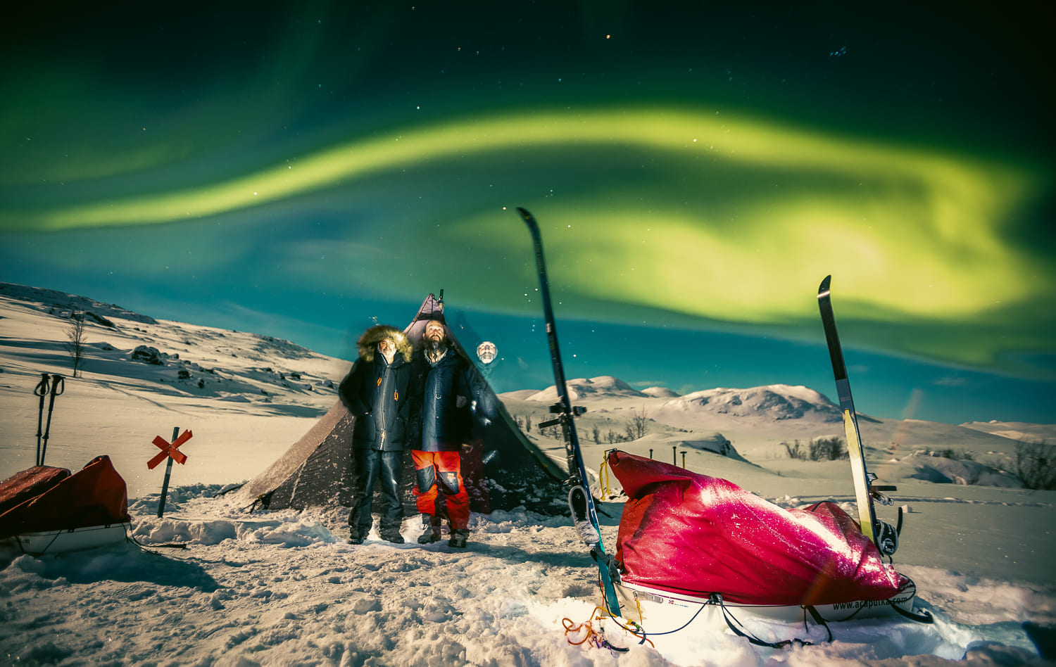 Expedicionarios junto a un tipi y pulkas bajo la aurora boreal en Laponia